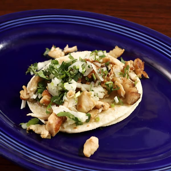A Sancho's Taqueria chicken taco, topped with cilantro and onions, on a blue plate.