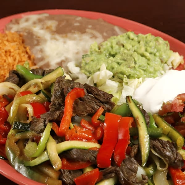 Sancho's Taqueria's sizzling fajitas with steak, colorful peppers, rice, beans, guacamole, and sour cream.