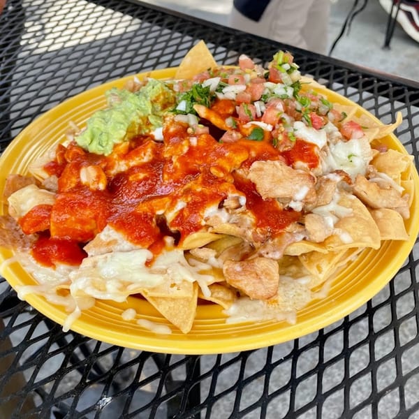 A vibrant yellow plate of Sancho's Taqueria nachos with chicken, red sauce, guacamole, and pico de gallo.