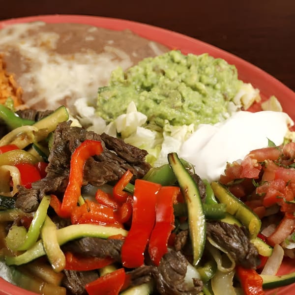 Sancho's Taqueria's sizzling fajitas with steak, peppers, onions, guacamole, sour cream, and refried beans.