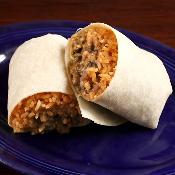 Two Sancho's Taqueria burritos, cut in half, revealing rice and meat filling on a blue plate.