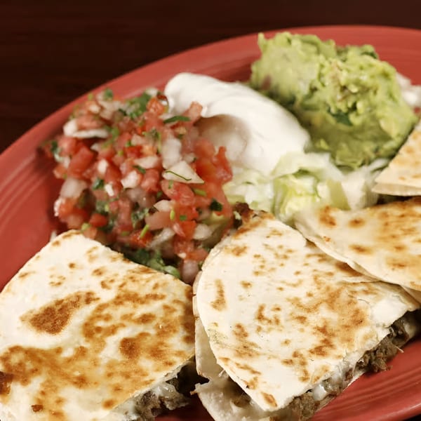 Sancho's Taqueria's quesadillas with guacamole, sour cream, pico de gallo, and lettuce on a red plate.