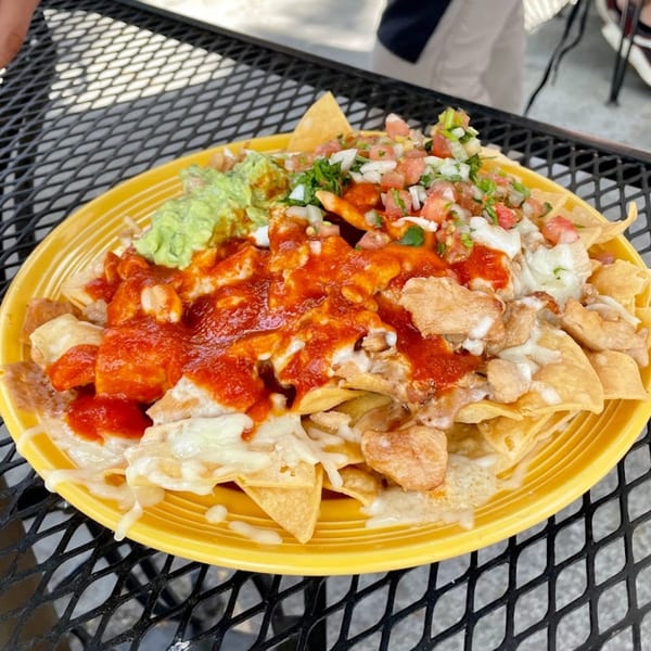 A vibrant plate of Sancho's Taqueria nachos with chicken, salsa, guacamole, and cheese sauce.