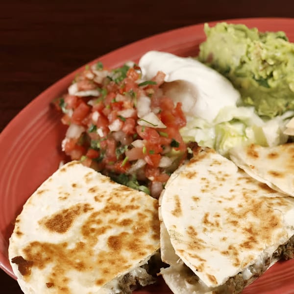 Sancho's Taqueria quesadillas with guacamole, pico de gallo, and sour cream on a red plate.