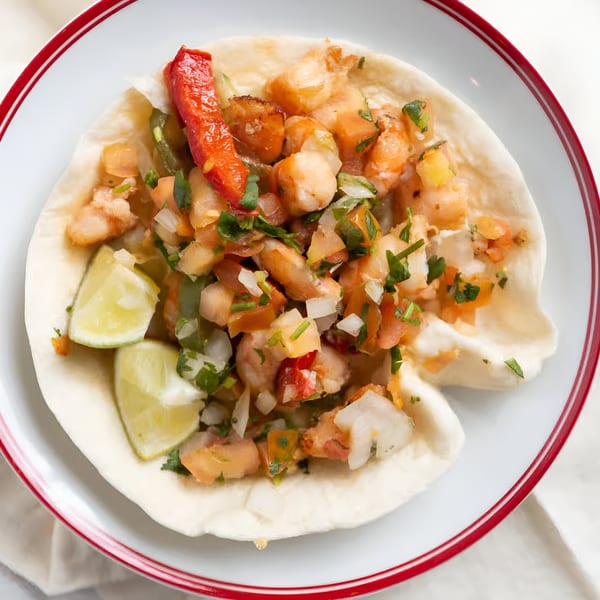 Sancho's Taqueria shrimp taco with pico de gallo, red pepper, and lime wedges on a white plate.