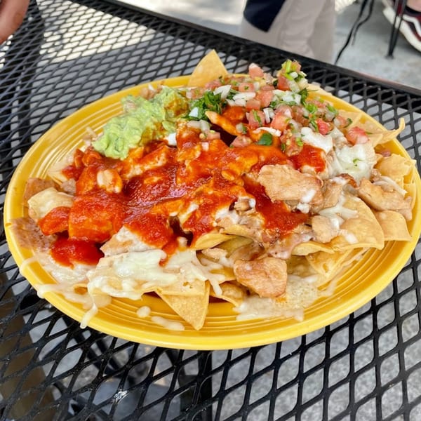 Sancho's Taqueria nachos with red sauce, cheese, guacamole, and pico de gallo on a yellow plate.