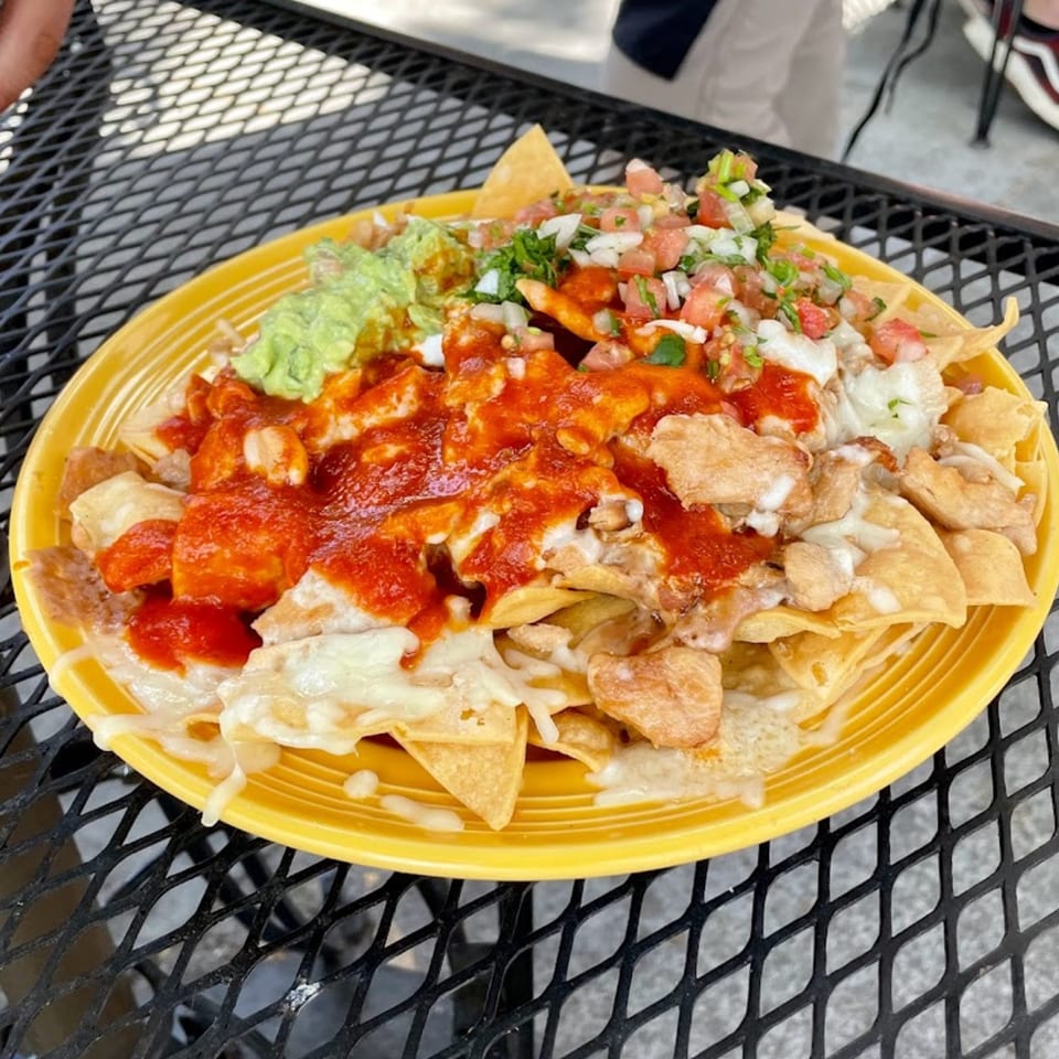 Sancho's Taqueria nachos with red sauce, cheese, guacamole, and pico de gallo on a yellow plate.